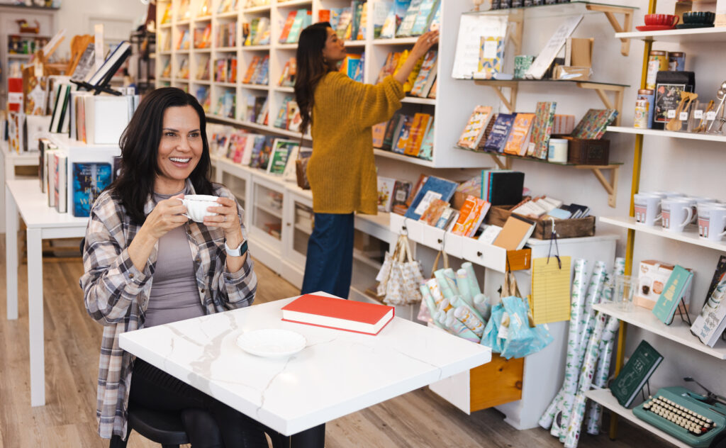 woman drinking cup of tea woman browsing books on shelf in background