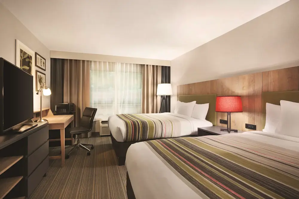 Large hotel room with two beds, desk, and entertainment center at Country Inn & Suites